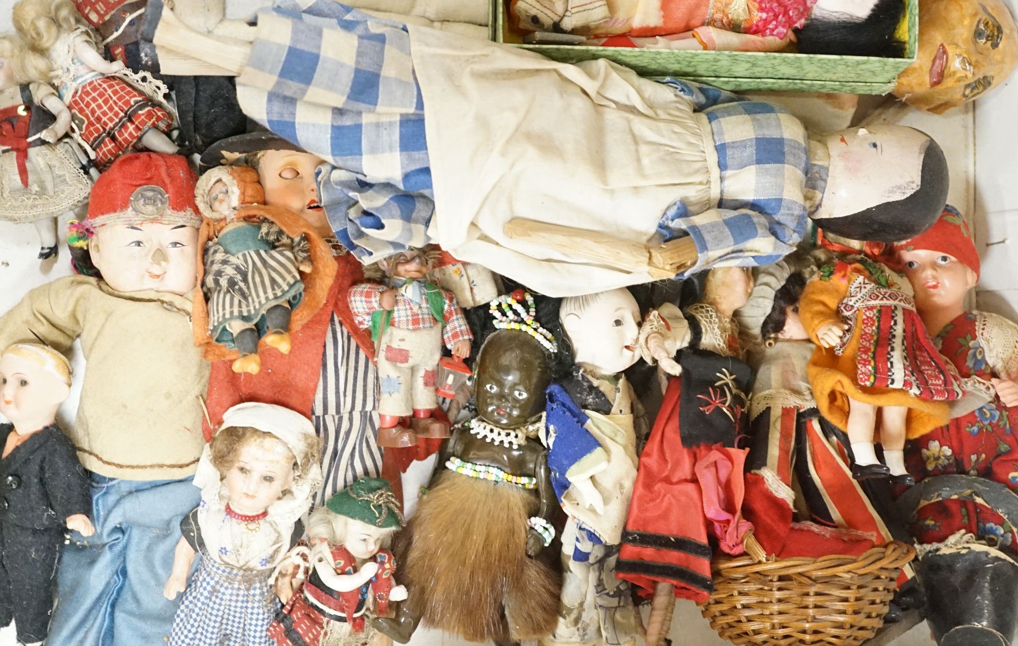 A quantity of bisque headed dolls,a collection of miniature and world dolls, a large bisque headed doll in a basket and a group of green dolls house wicker furniture
